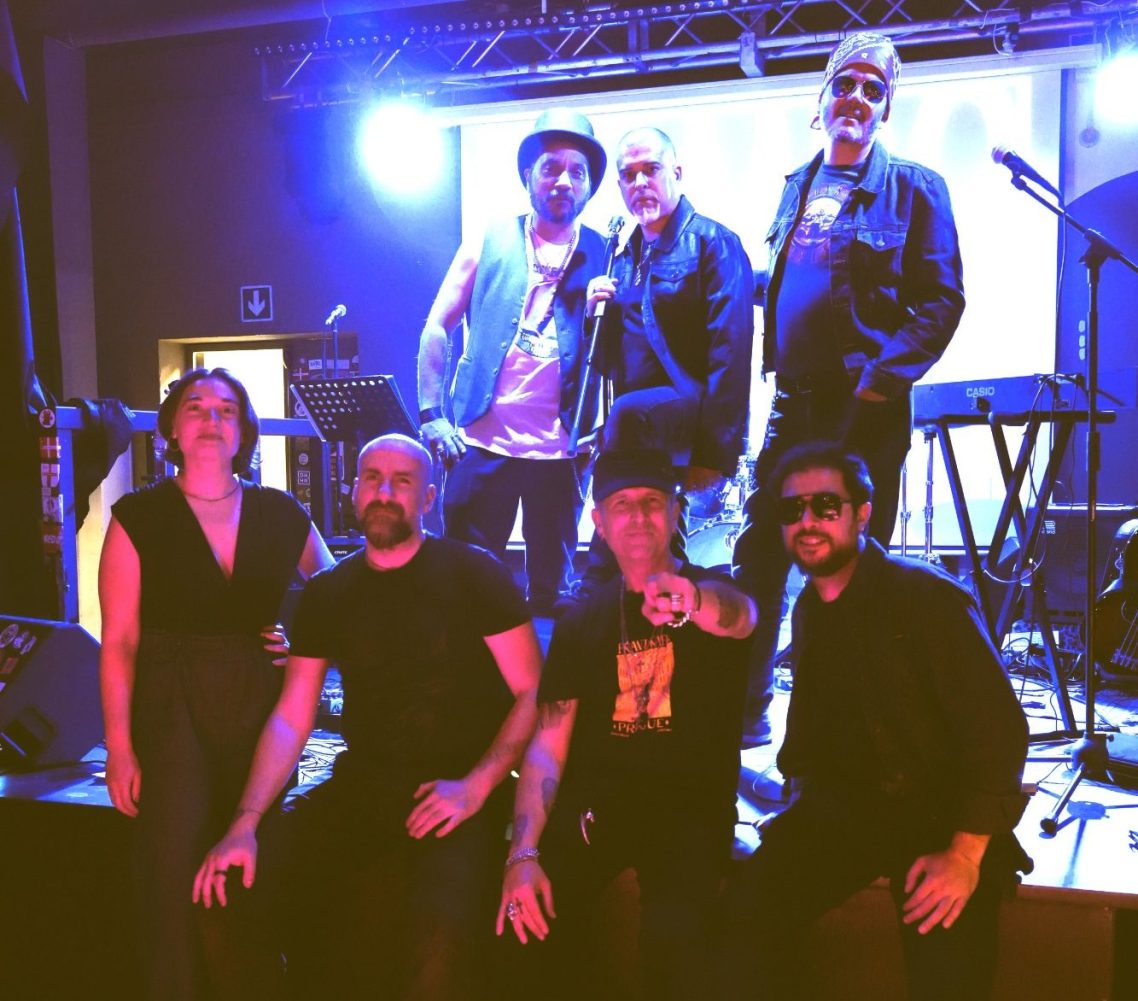 Una band su un palco, esibendosi con diversi strumenti musicali di fronte a un pubblico.